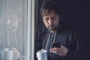 a man by the window checking his phone email with a cup in his hand